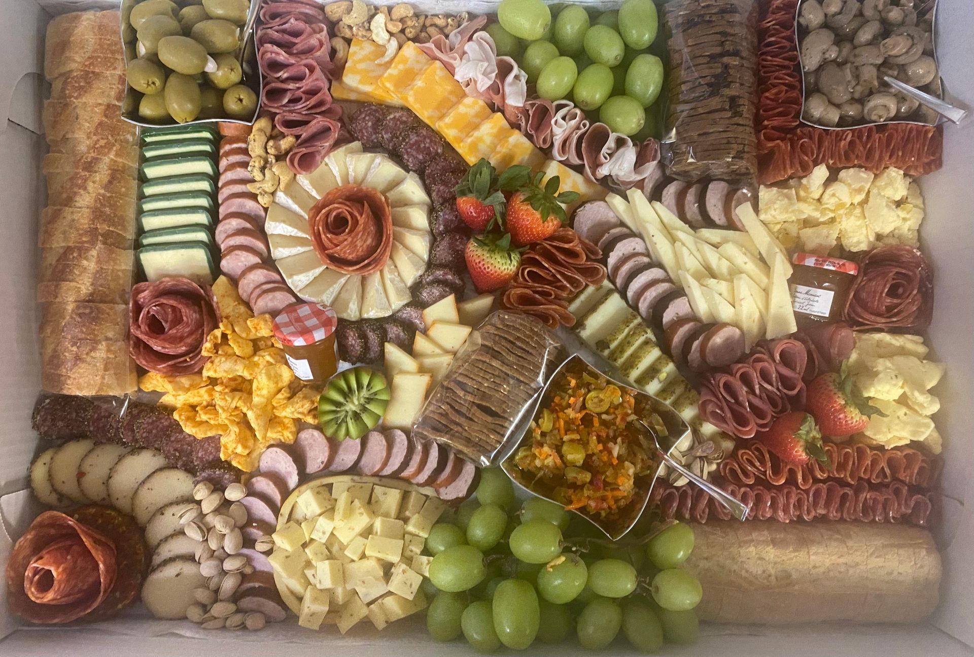 Charcuterie board with grapes, meats, cheeses, crackers, nuts, and dried fruit arranged in a festive pattern