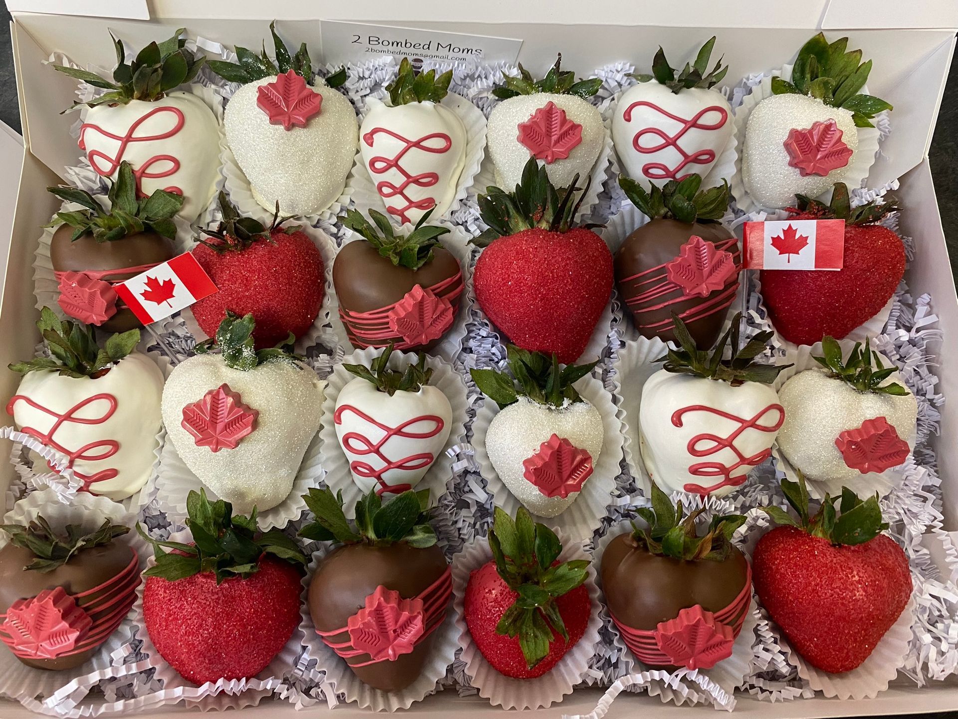 Assorted chocolate-dipped strawberries in red, white, and brown, arranged in a tray with maple leaf decorations