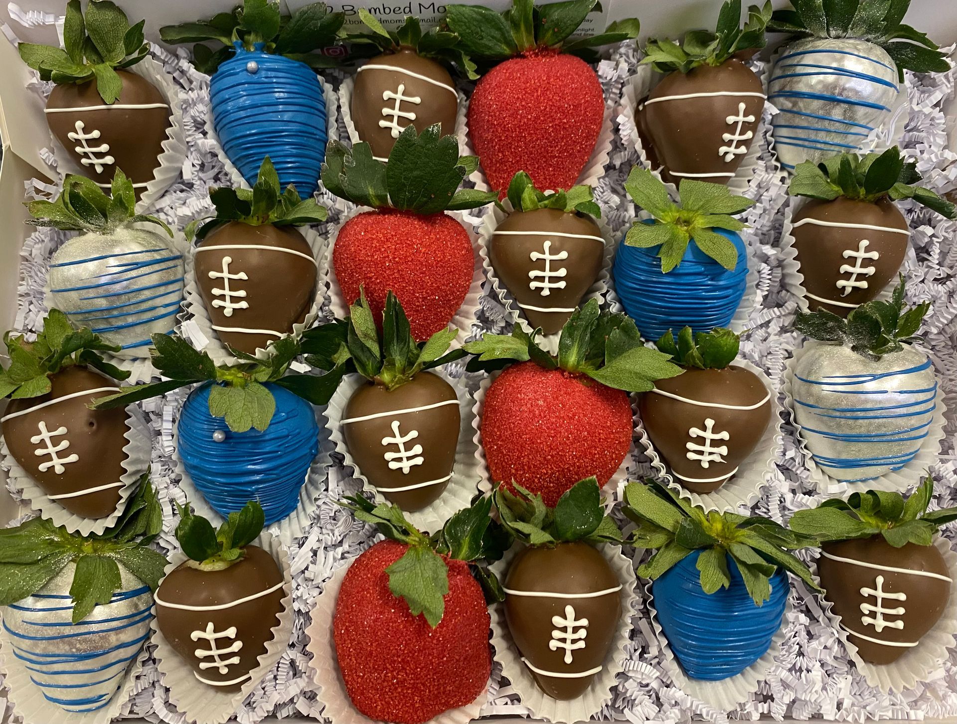 Chocolate-covered strawberries arranged like footballs, mixed with red strawberries and blue and white decorated berries.