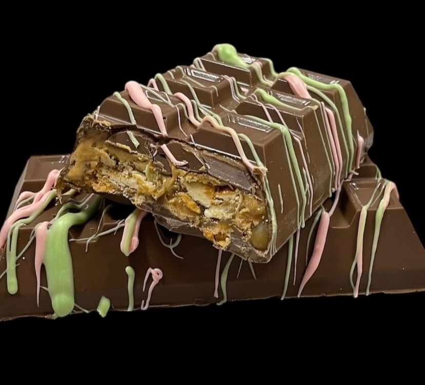 Chocolate-covered candy bars stacked with drizzled pink and green icing on a black background