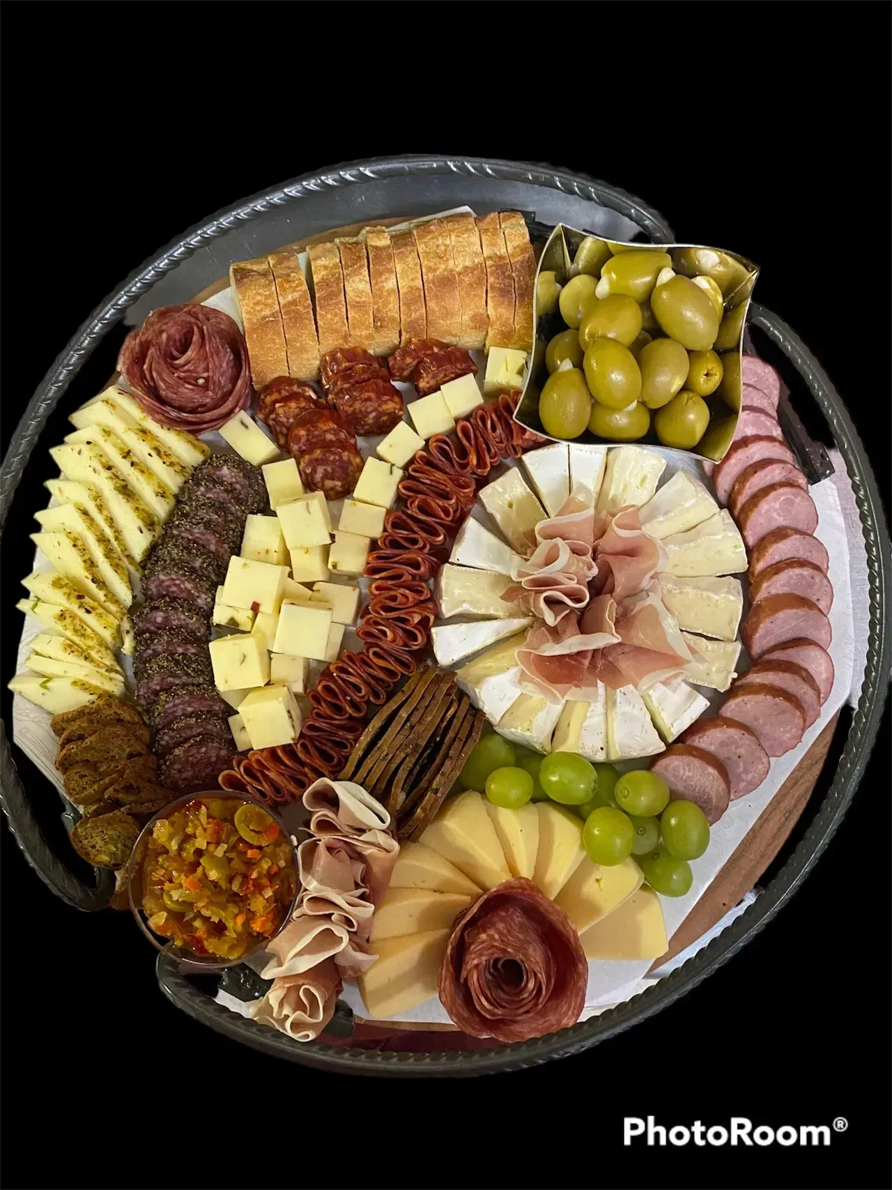 Charcuterie board with assorted cheeses, meats, crackers, olives, grapes, and spreads arranged on a round platter