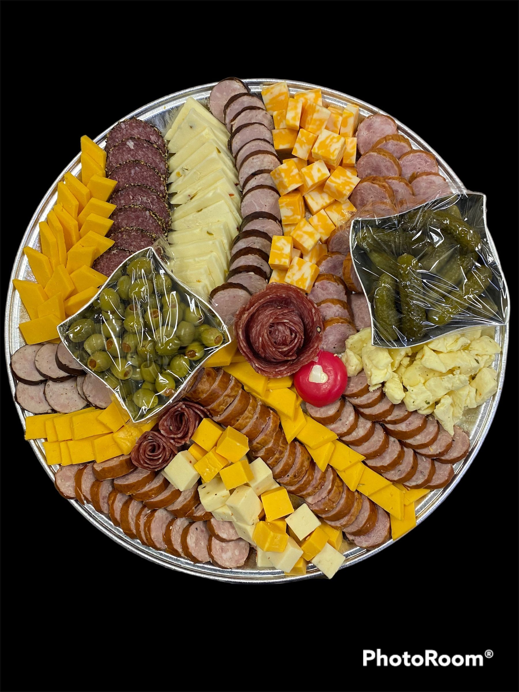 Round charcuterie board with meats, cheeses, crackers, olives, and fruit arranged in a spiral pattern.