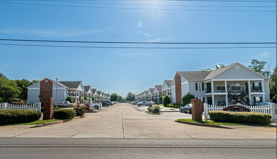 Wide residential street lined with white houses and brick pillars under a clear blue sky