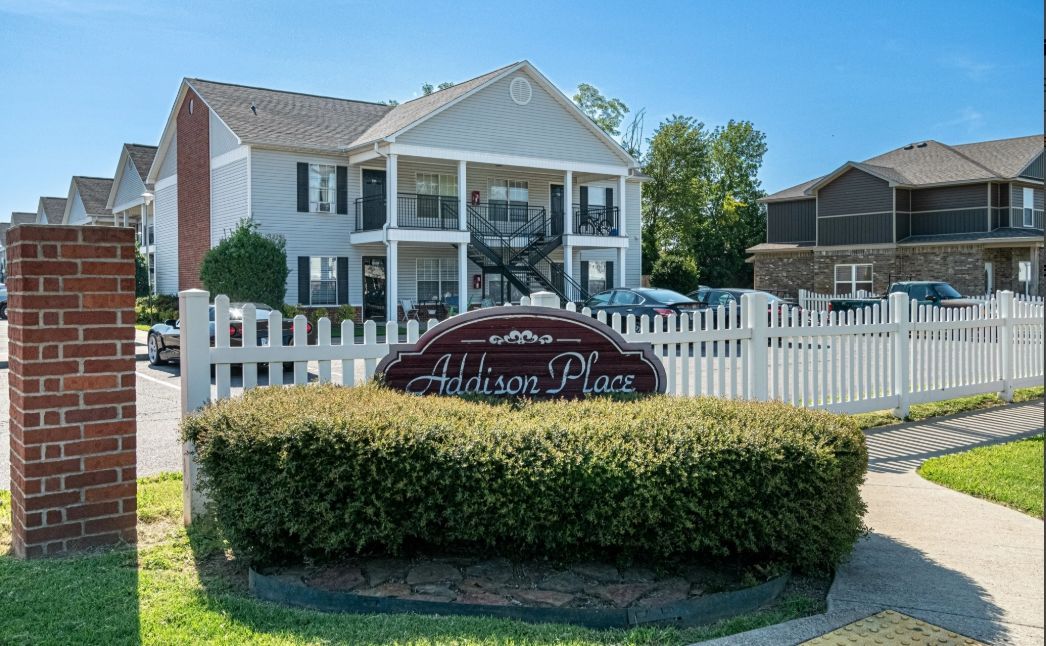 Entrance sign and white picket fence in front of suburban townhouses on a sunny day