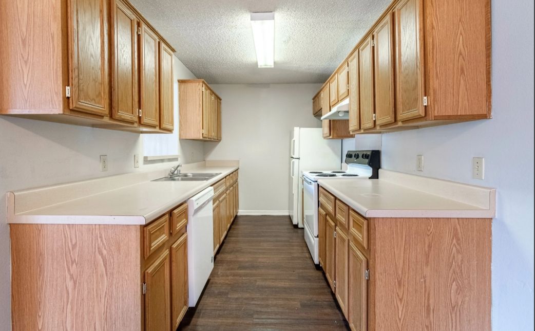 Empty galley kitchen with wood cabinets, white counters, and dark flooring.