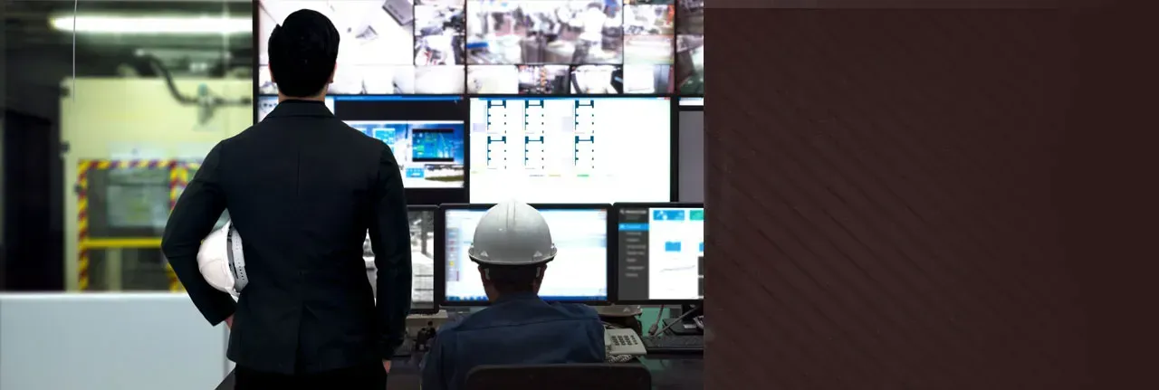 A man in a suit and hard hat is standing in front of a computer monitor.