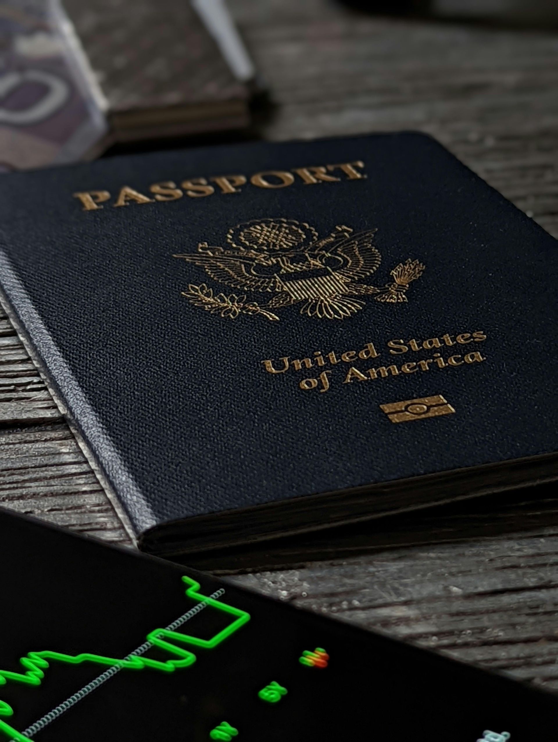A passport is sitting on a wooden table next to a cell phone.
