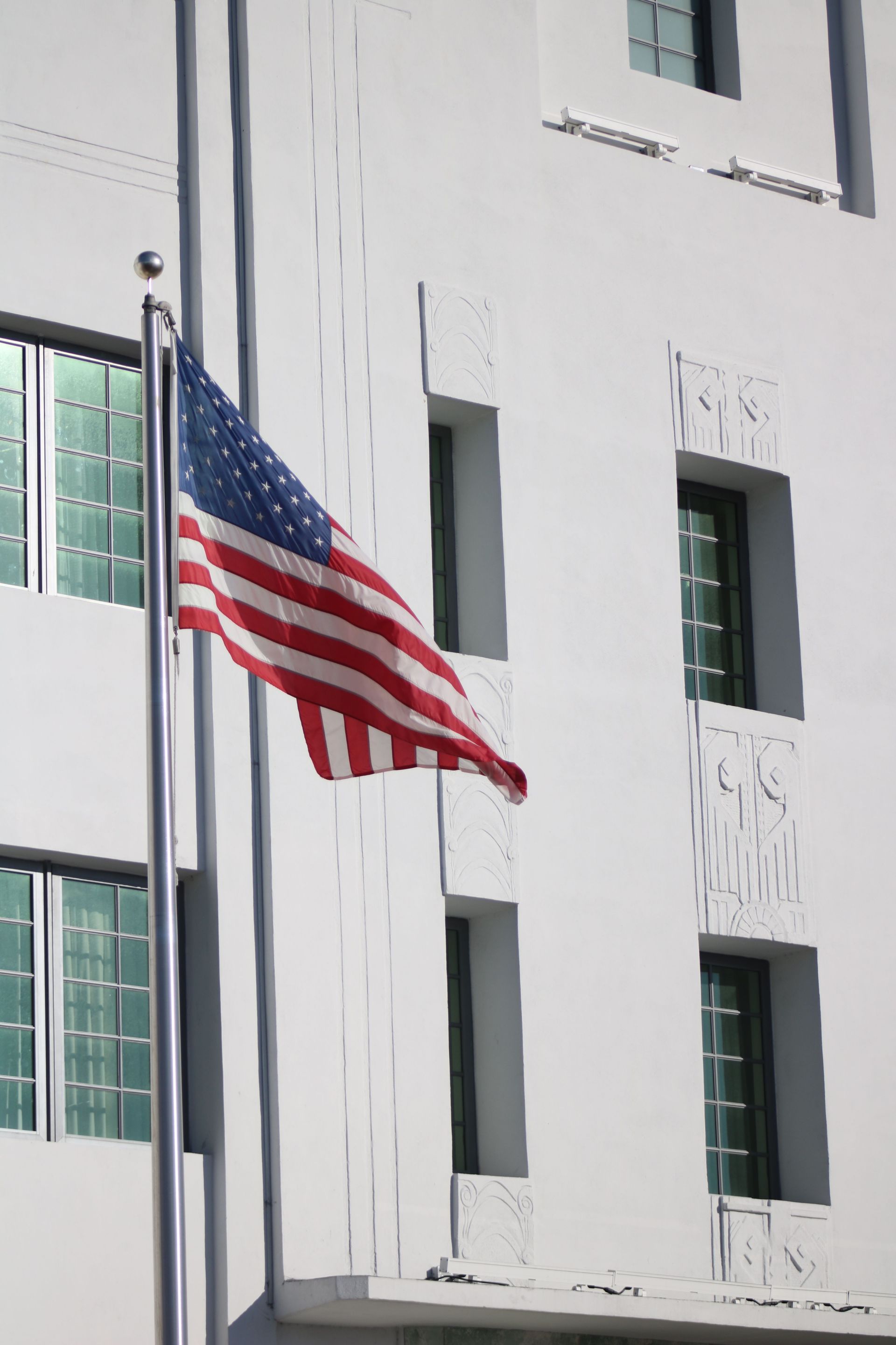 American flag hanging outside a white building with green windows