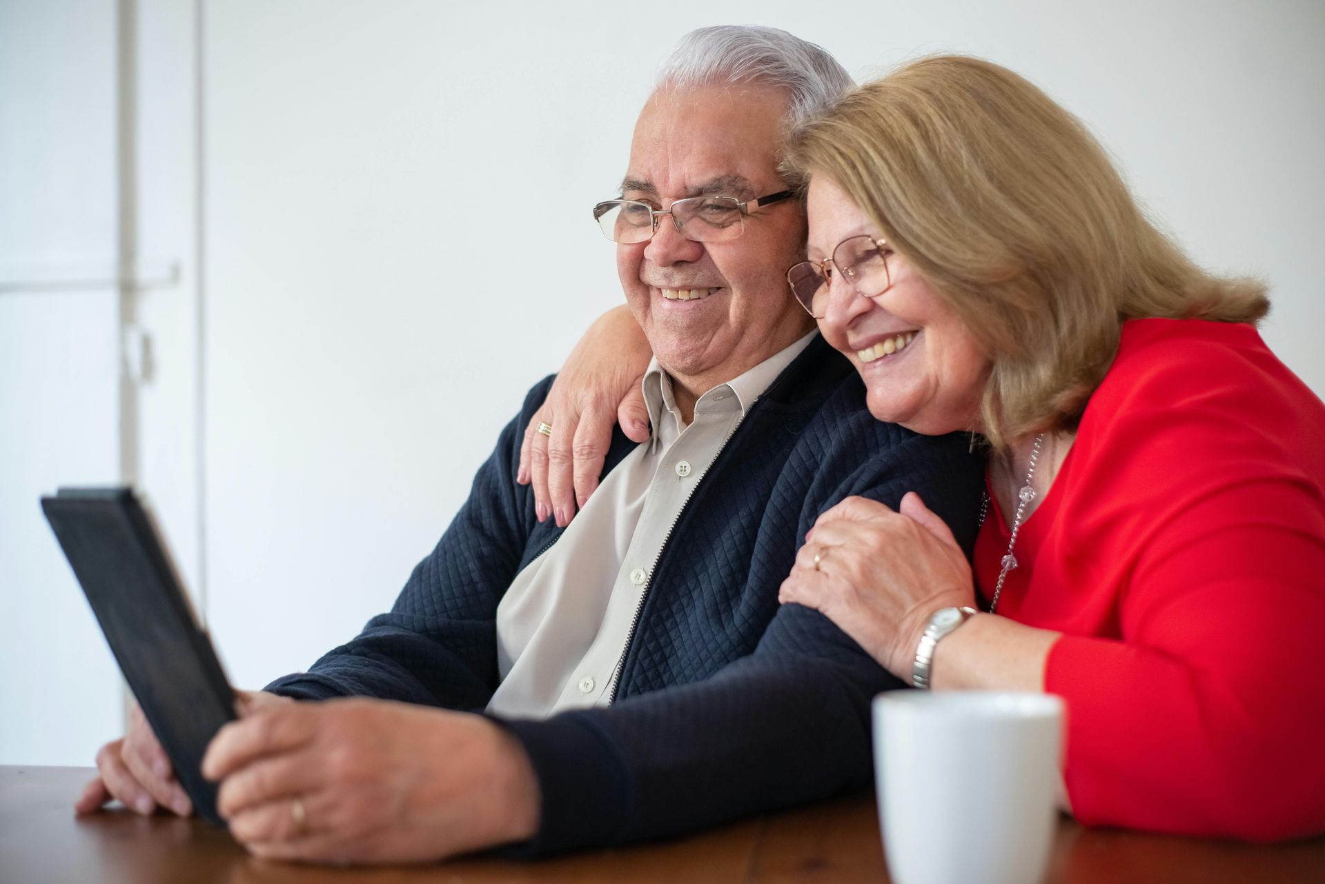 Smiling couple looks at tablet together, one arm around the other.