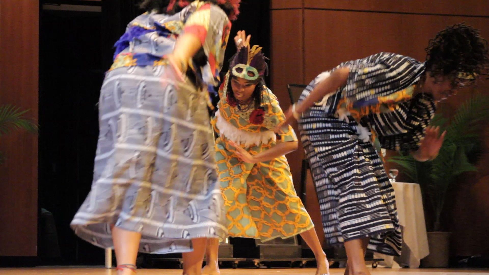 Three dancers in colorful patterned clothing perform on stage.