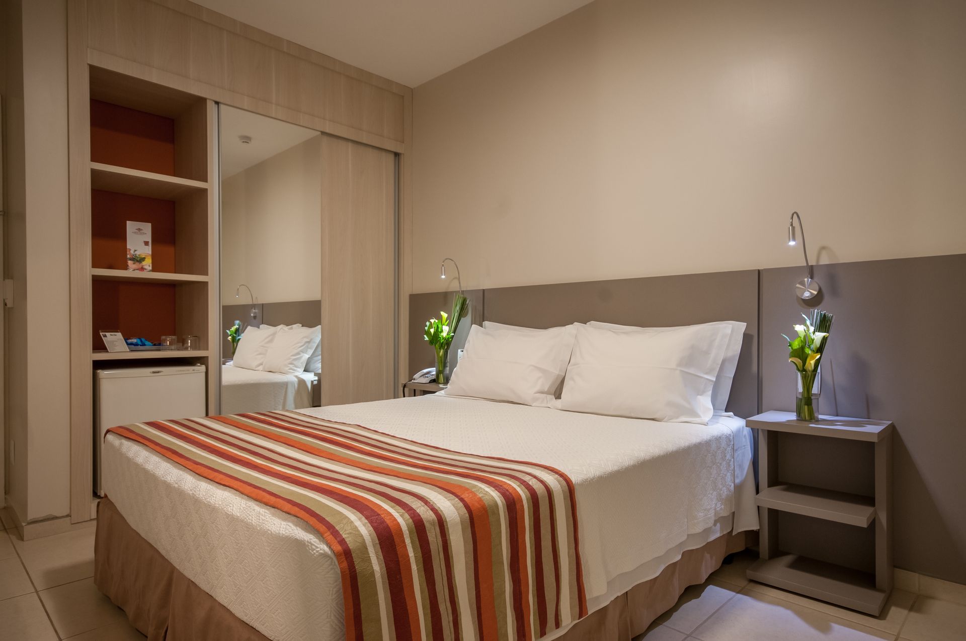Um quarto de hotel com uma cama, mesa de cabeceira e espelho.
