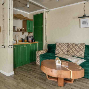 A cozy living area featuring a green sofa, wooden coffee table, and an adjacent kitchen with green cabinets.