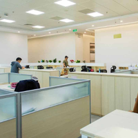 A bright, modern open-plan office with rows of cubicle desks, neutral furniture, and a few people working at computers.