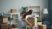 A beige two-car garage with white trim and a brown shingle roof under a clear blue sky.
