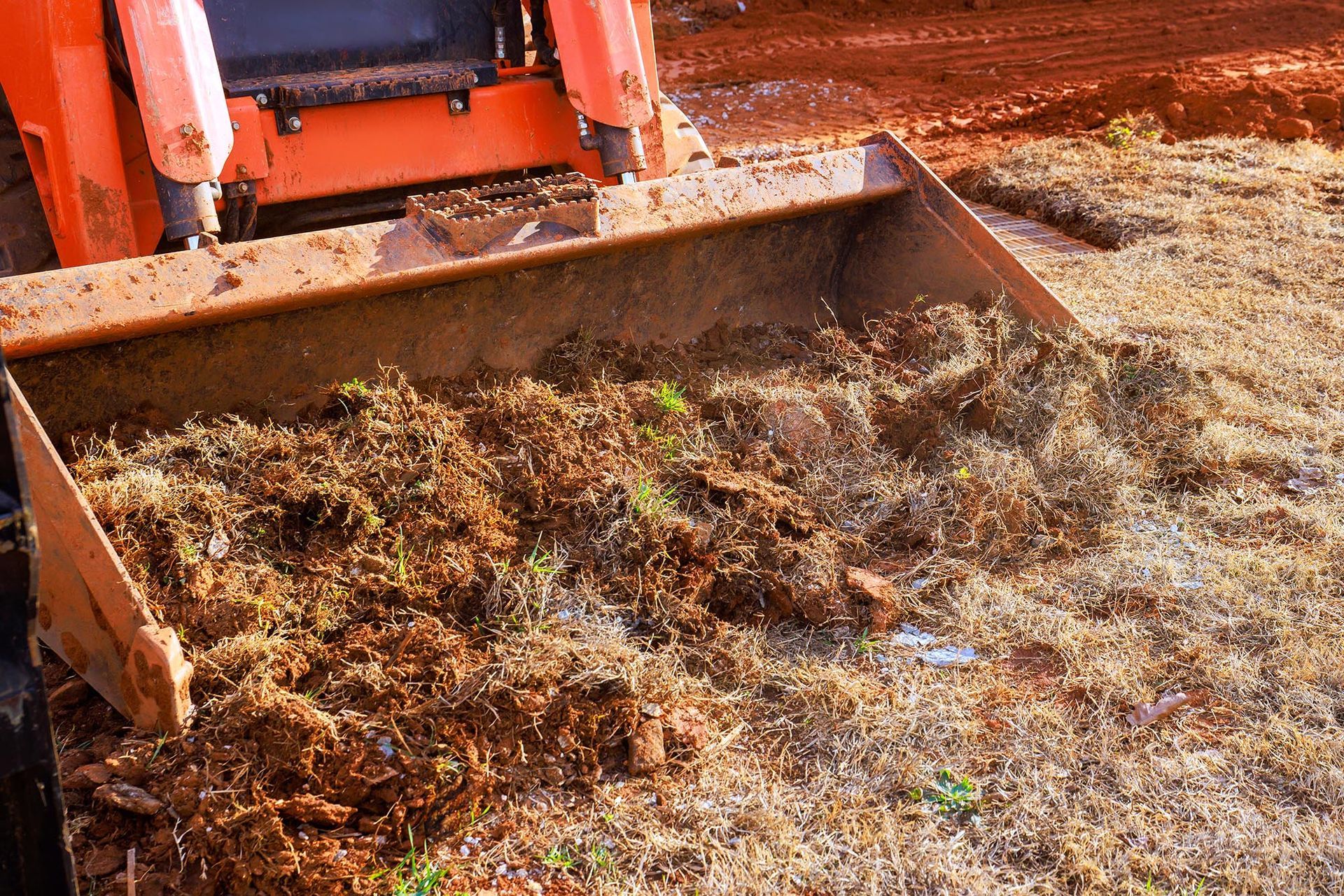 Orange construction loader pushing a pile of dirt and debris on a muddy ground