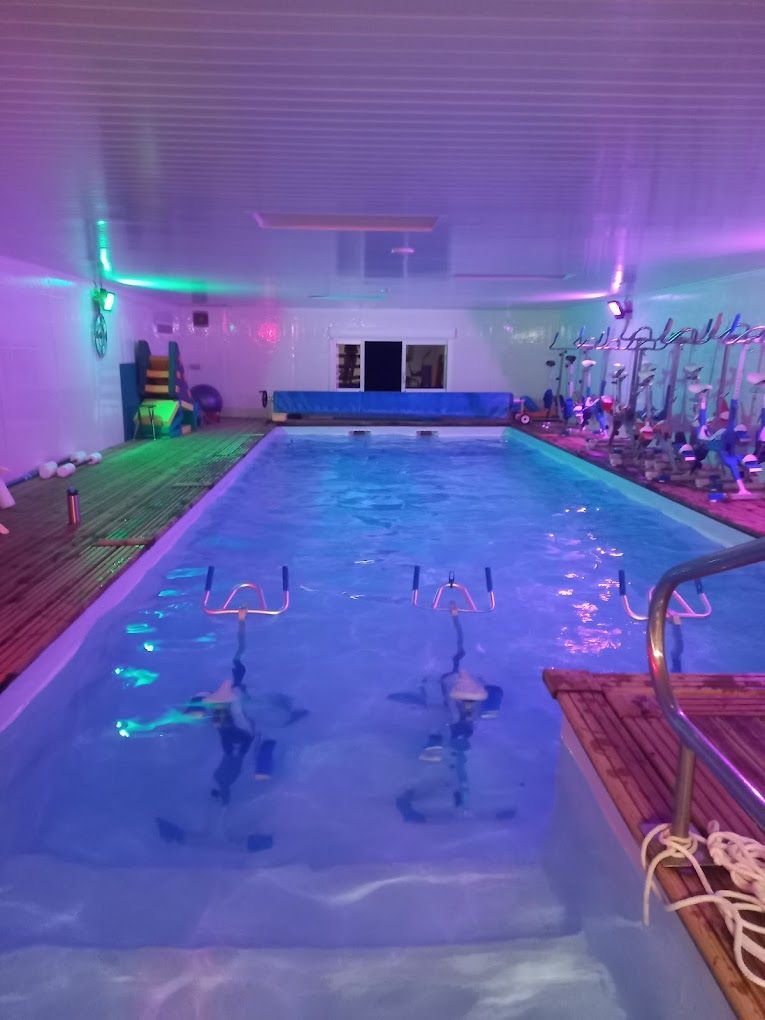 Piscine intérieure éclairée de lumières bleues et violettes, l'eau ondulant doucement la nuit