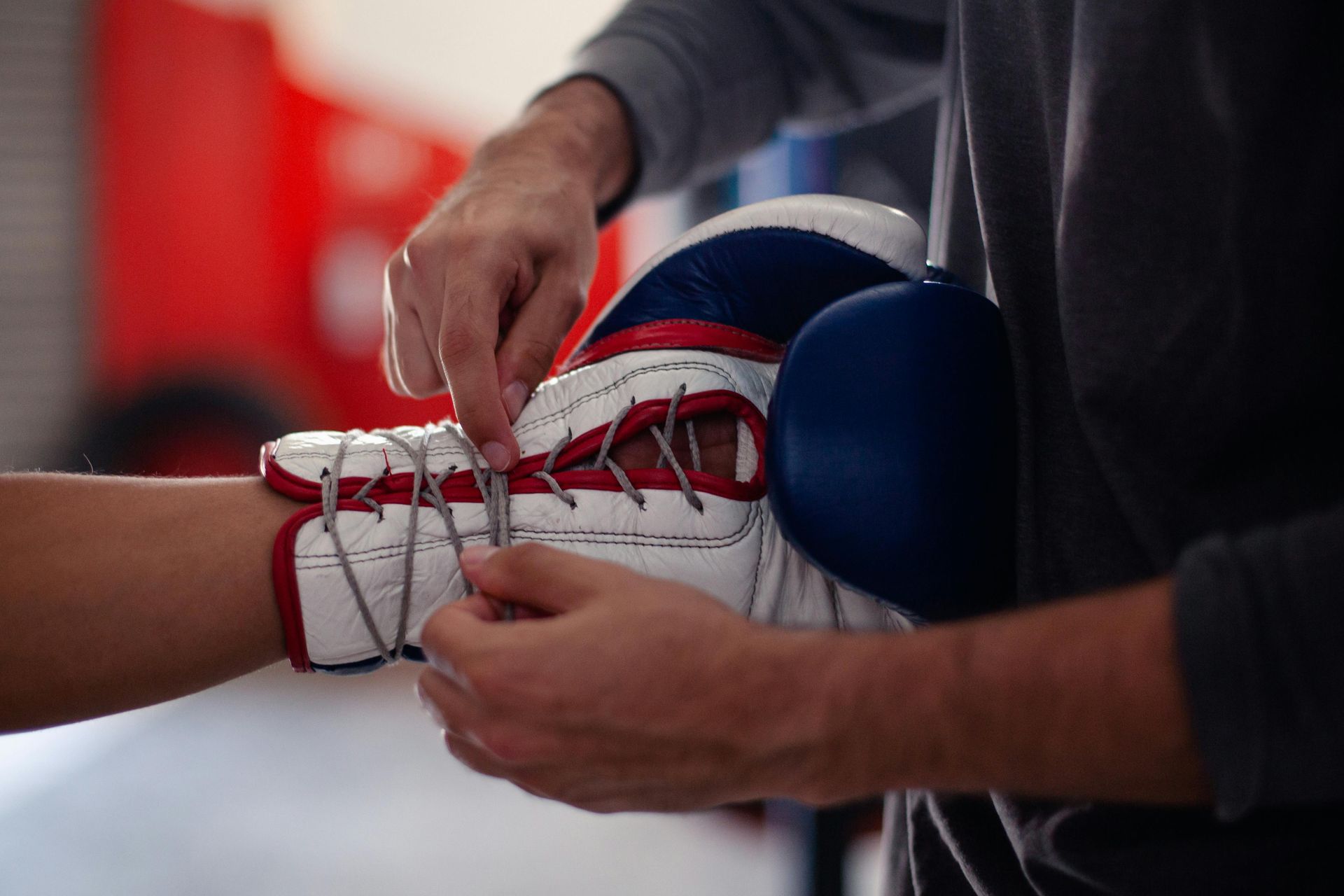 Des mains nouent des lacets rouges sur une chaussure de boxe blanche