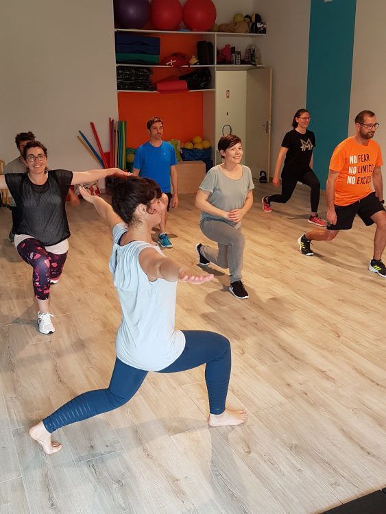 Cours de fitness en groupe dans un studio, avec des participants faisant des fentes sur un parquet.