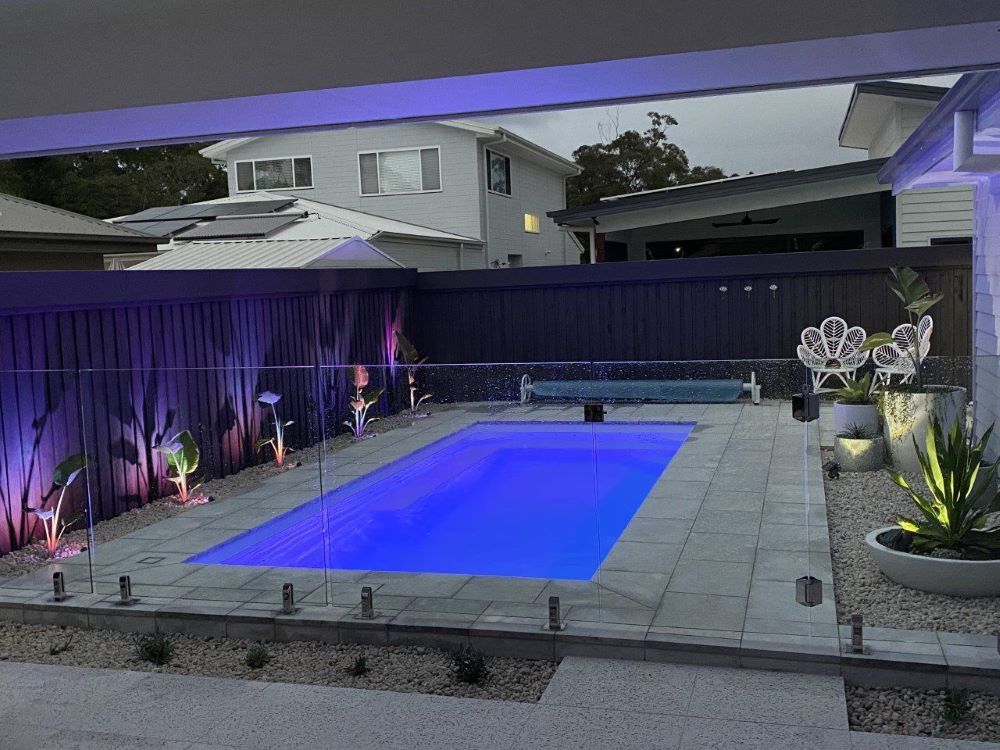 A Large Swimming Pool is Lit Up at Night With Purple Lights — Clarence Valley Pools In Grafton, NSW