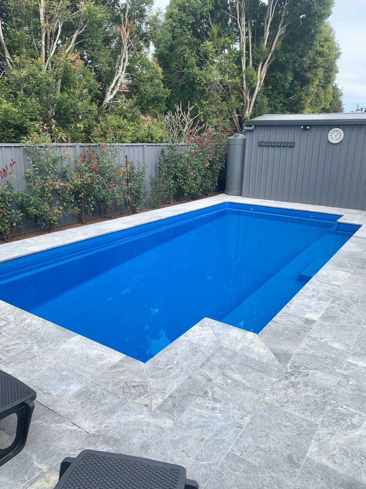Rectangular blue swimming pool in a paved backyard with surrounding greenery and a gray storage shed — Clarence Valley Pools In Yamba, NSW