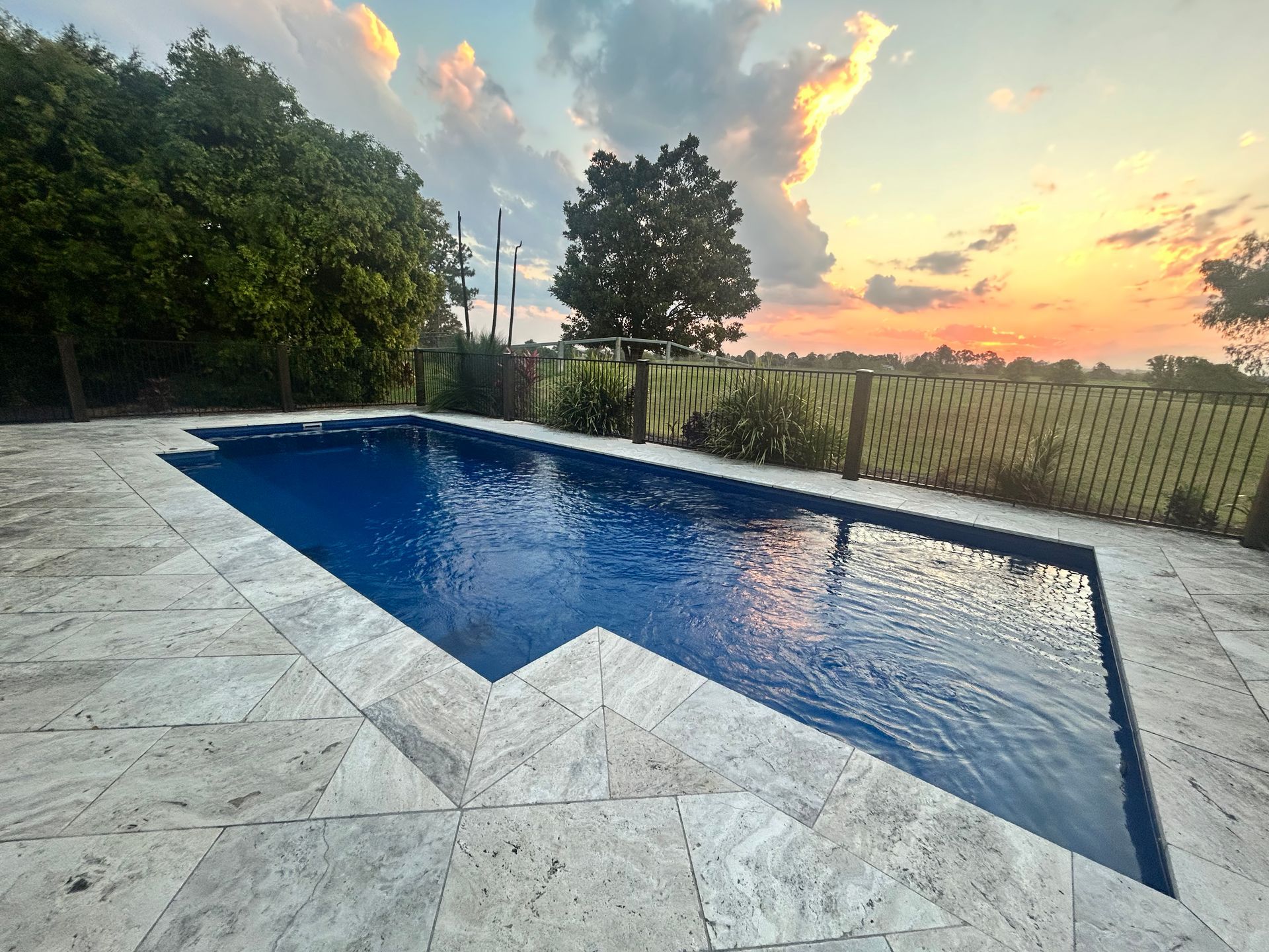 Swimming pool with blue water and stone patio at sunset — Clarence Valley Pools In Yamba, NSW