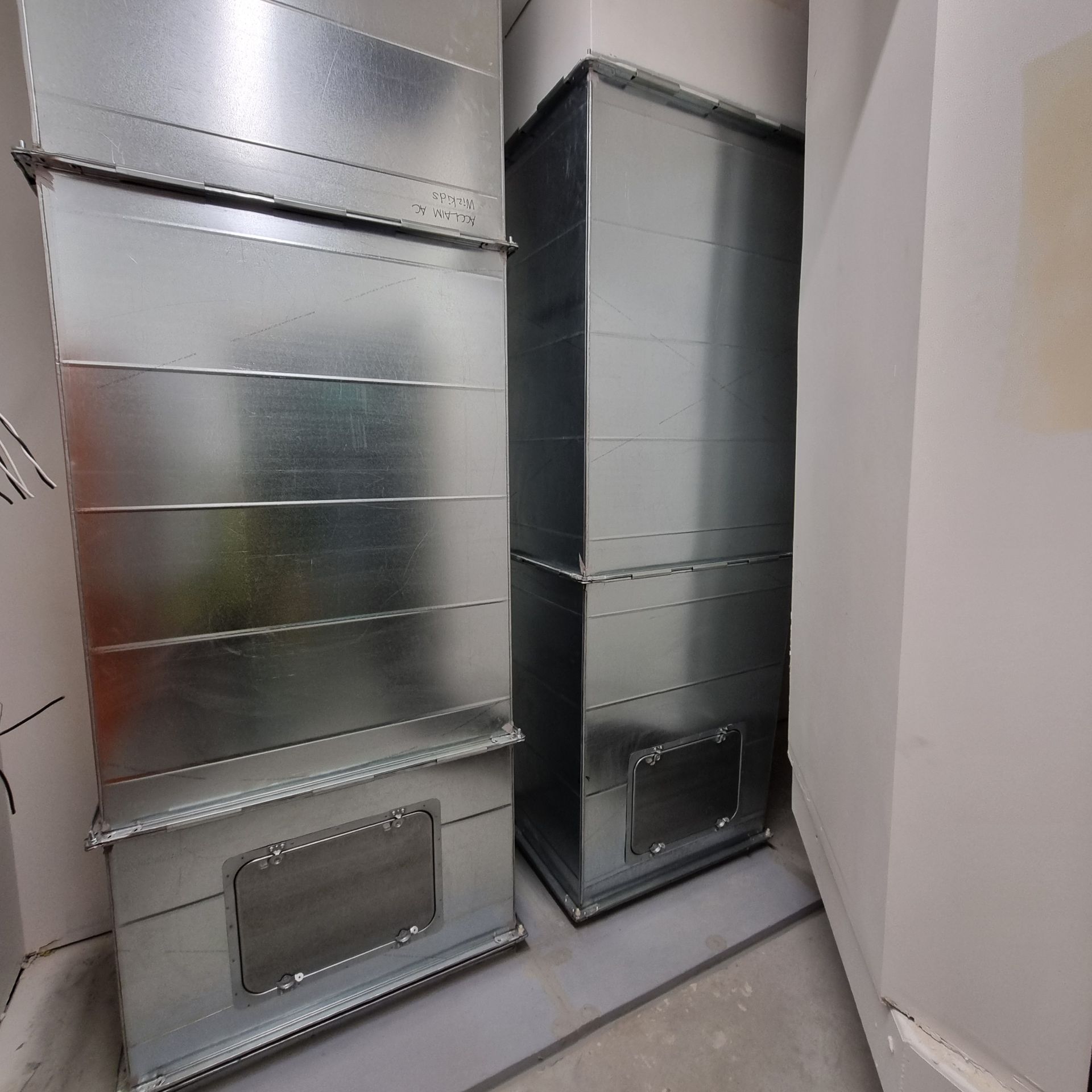 Two tall silver metal HVAC ducts in a narrow indoor utility space