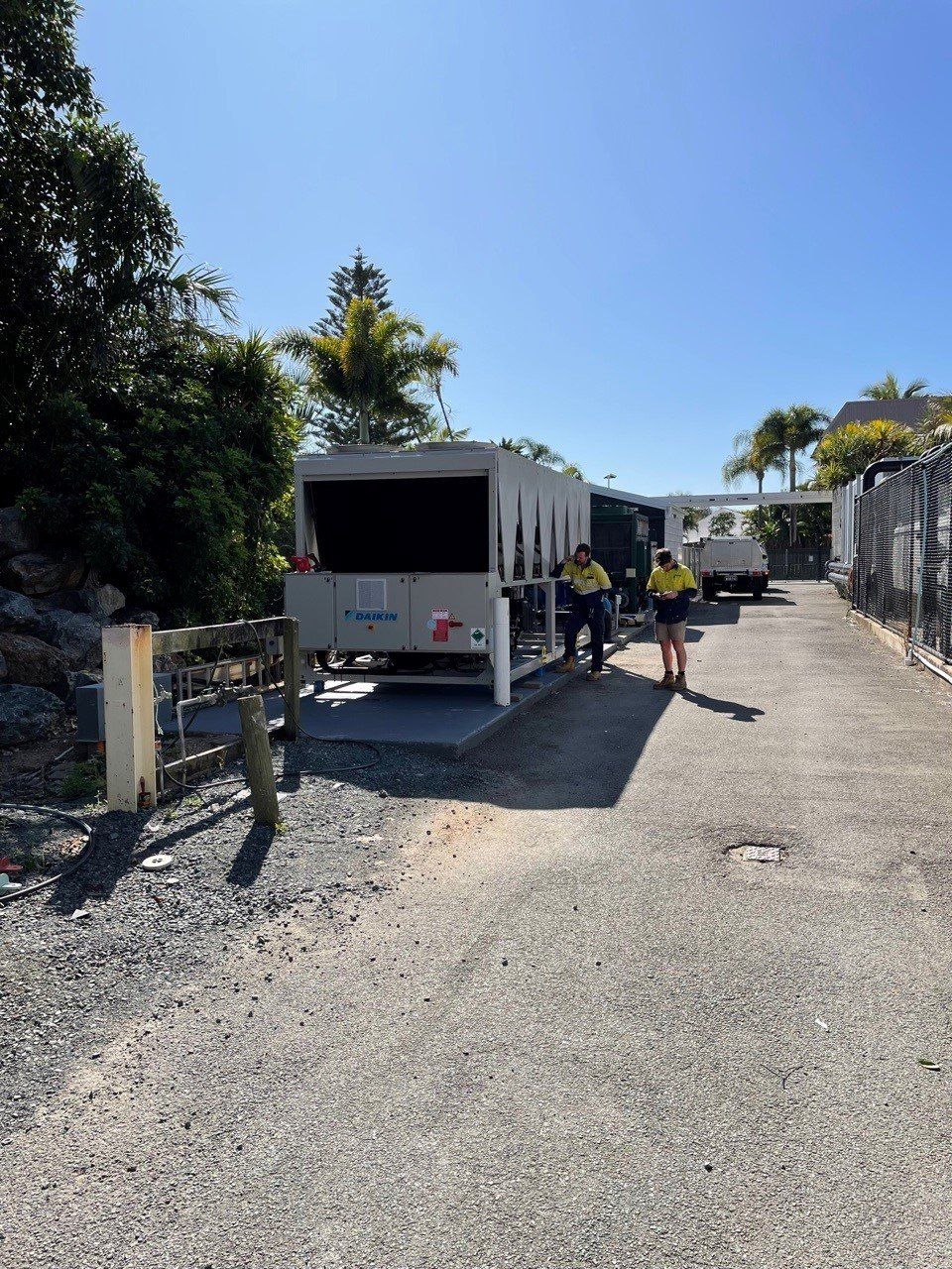 Outdoor gravel driveway with a parked white utility trailer and people loading items in bright sunlight