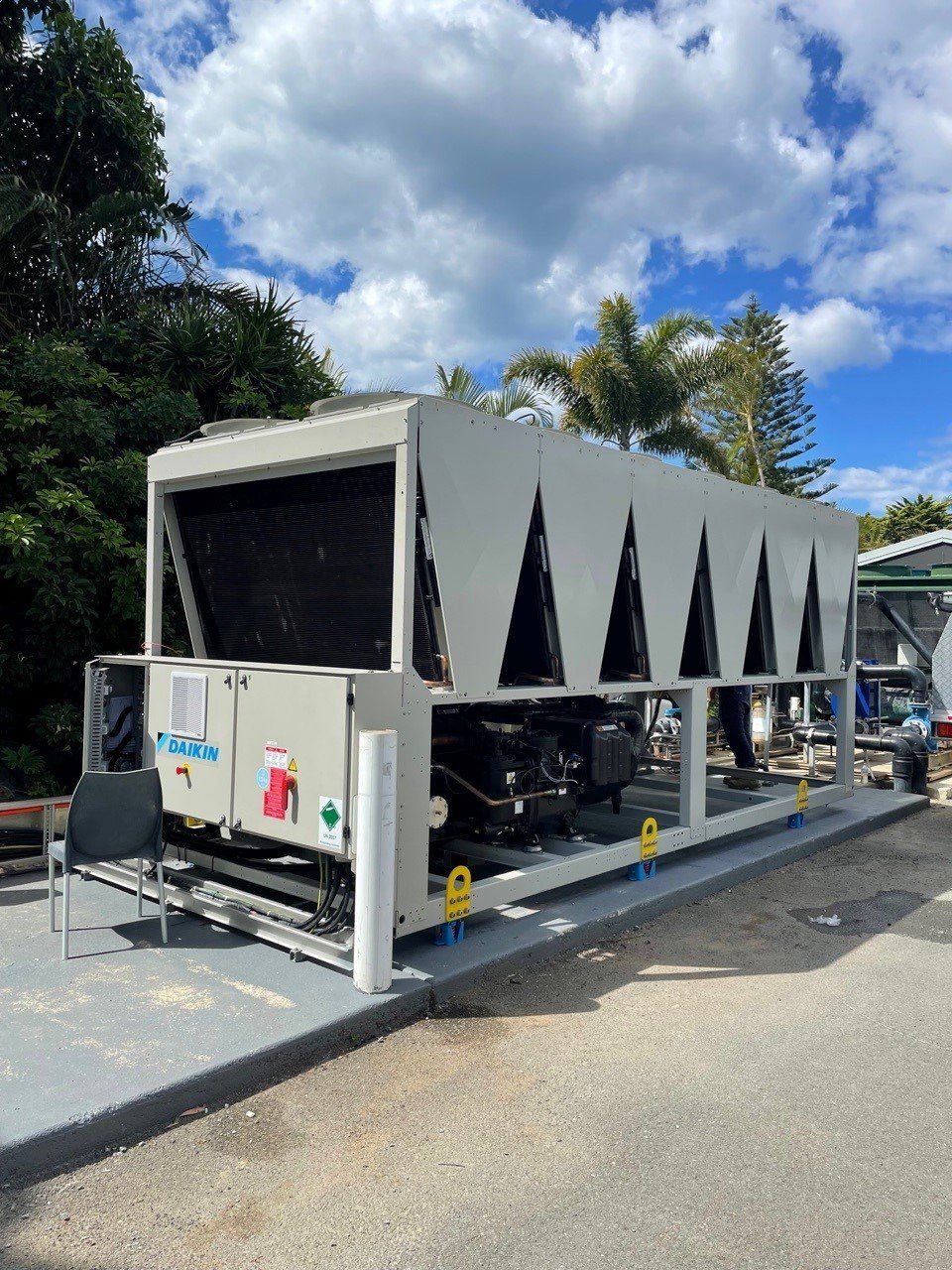 Large gray industrial machine trailer parked outdoors on a road, with black triangular vents and trees in the background