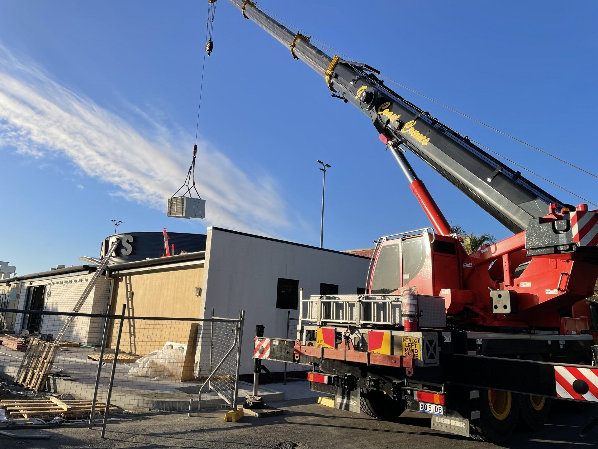 Crane lifting materials beside a building under construction on a sunny day