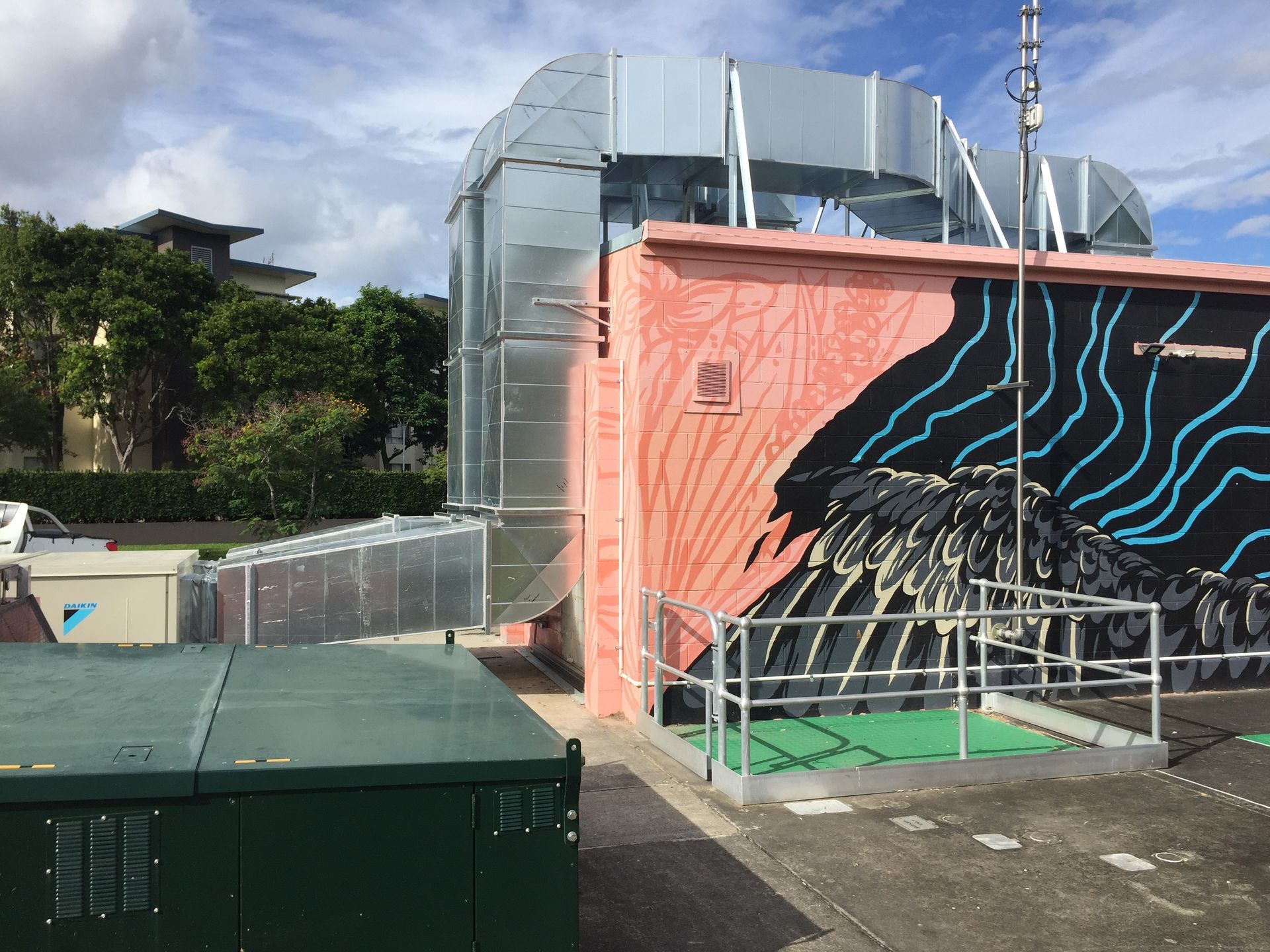 Colorful mural on a building beside industrial rooftop equipment under a cloudy sky