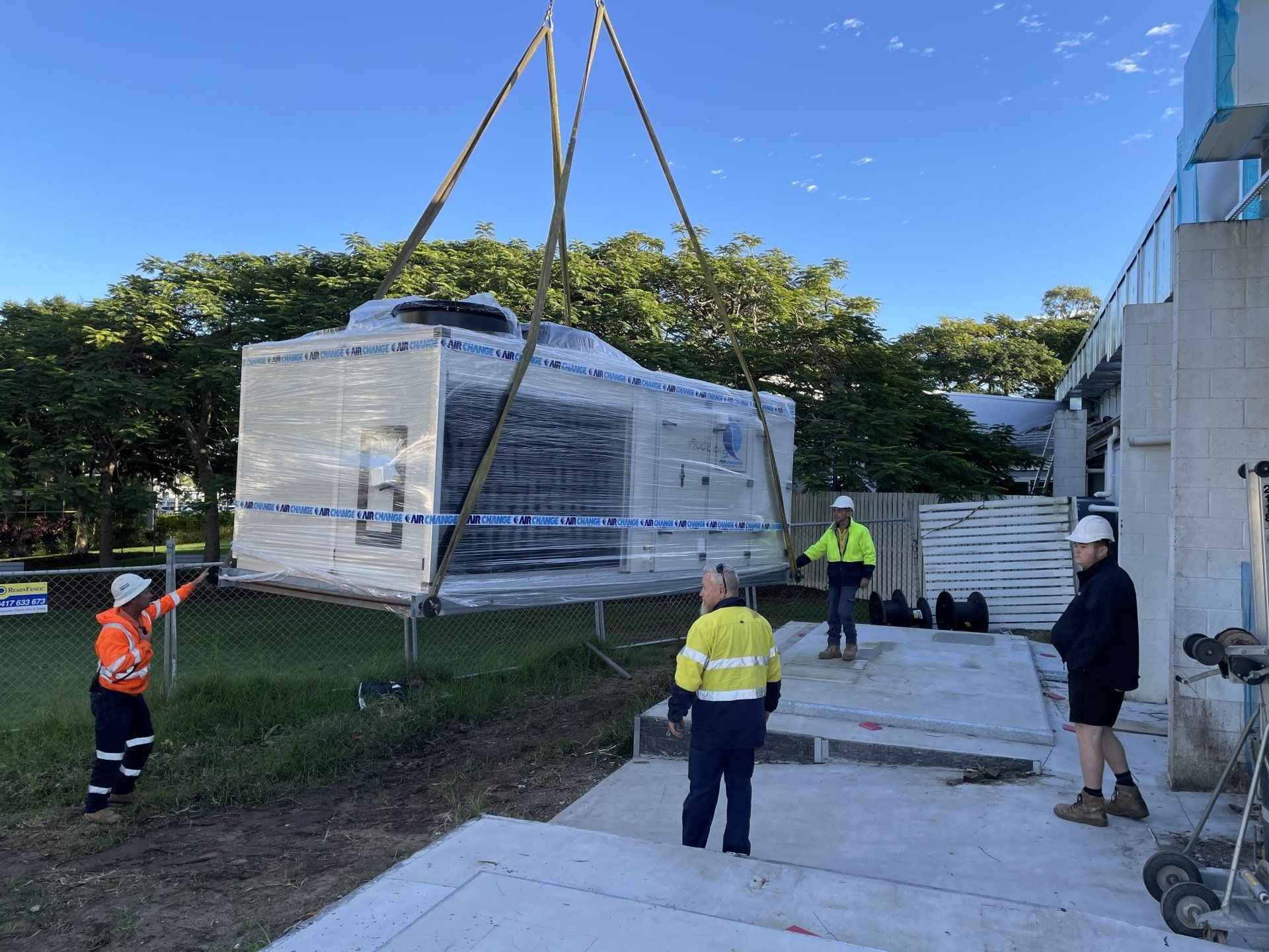 Crane lifts a wrapped modular building onto a site, with workers guiding the installation.