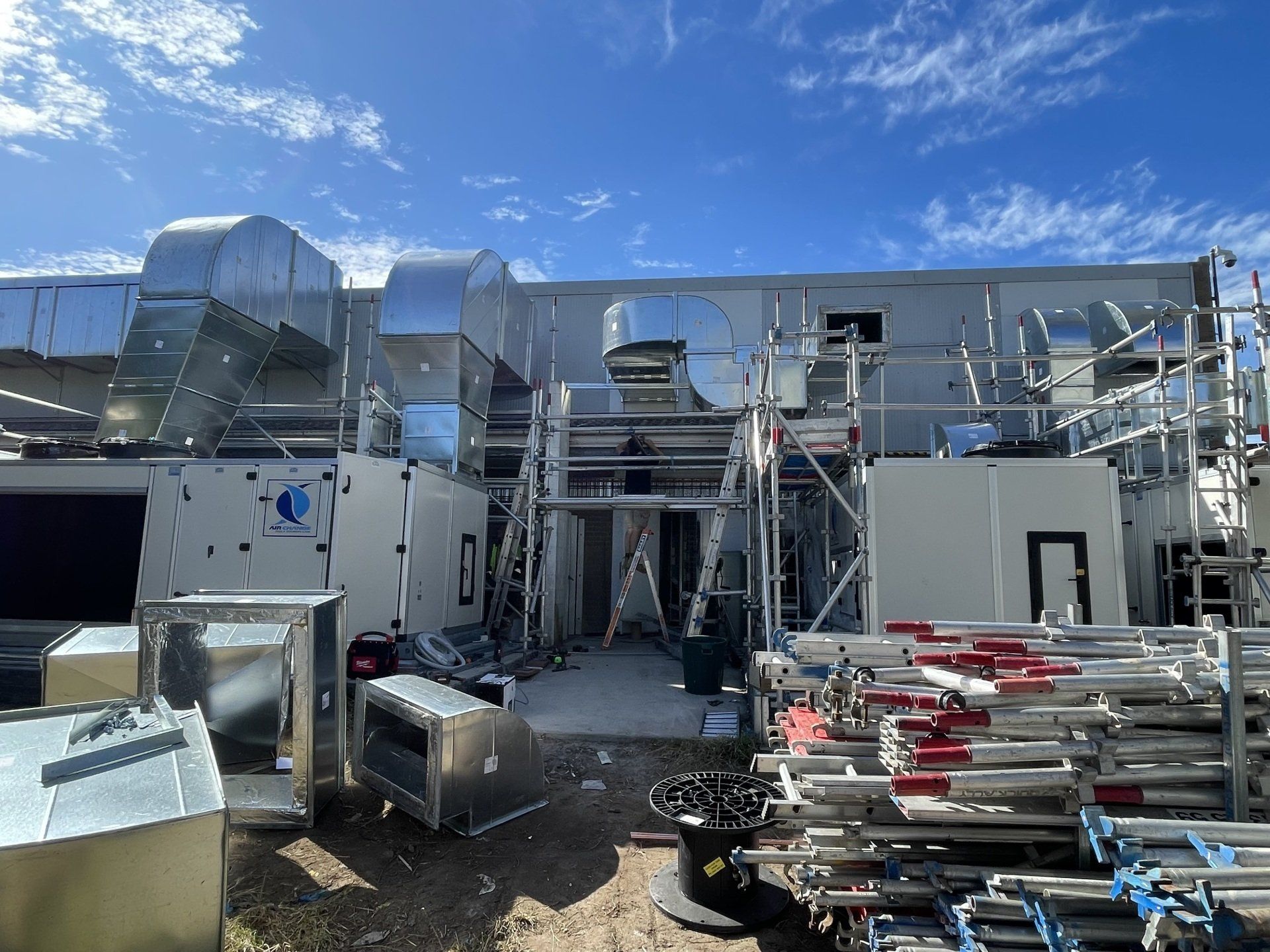 Industrial rooftop with HVAC units, ductwork, and stacked metal equipment under a blue sky