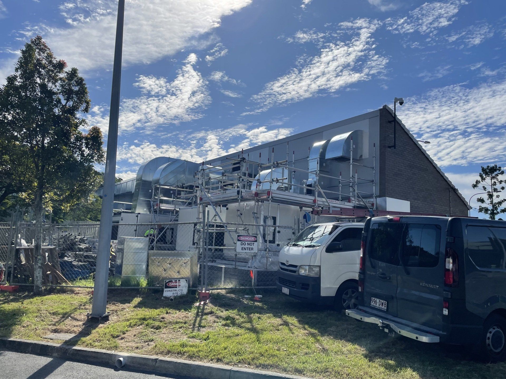 Damaged building with torn roof panels, parked vans, and construction debris under a bright blue sky