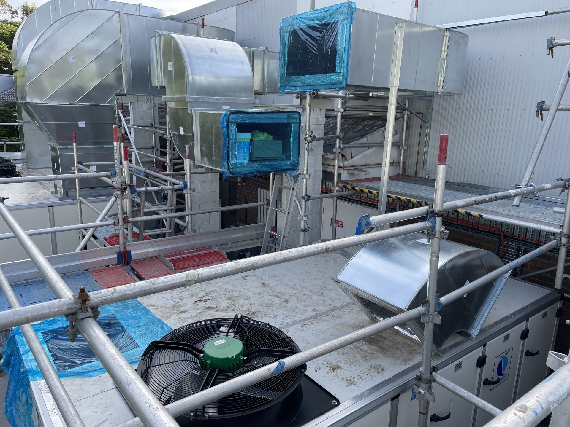 Industrial rooftop ventilation units and ductwork with blue insulation and metal railings.