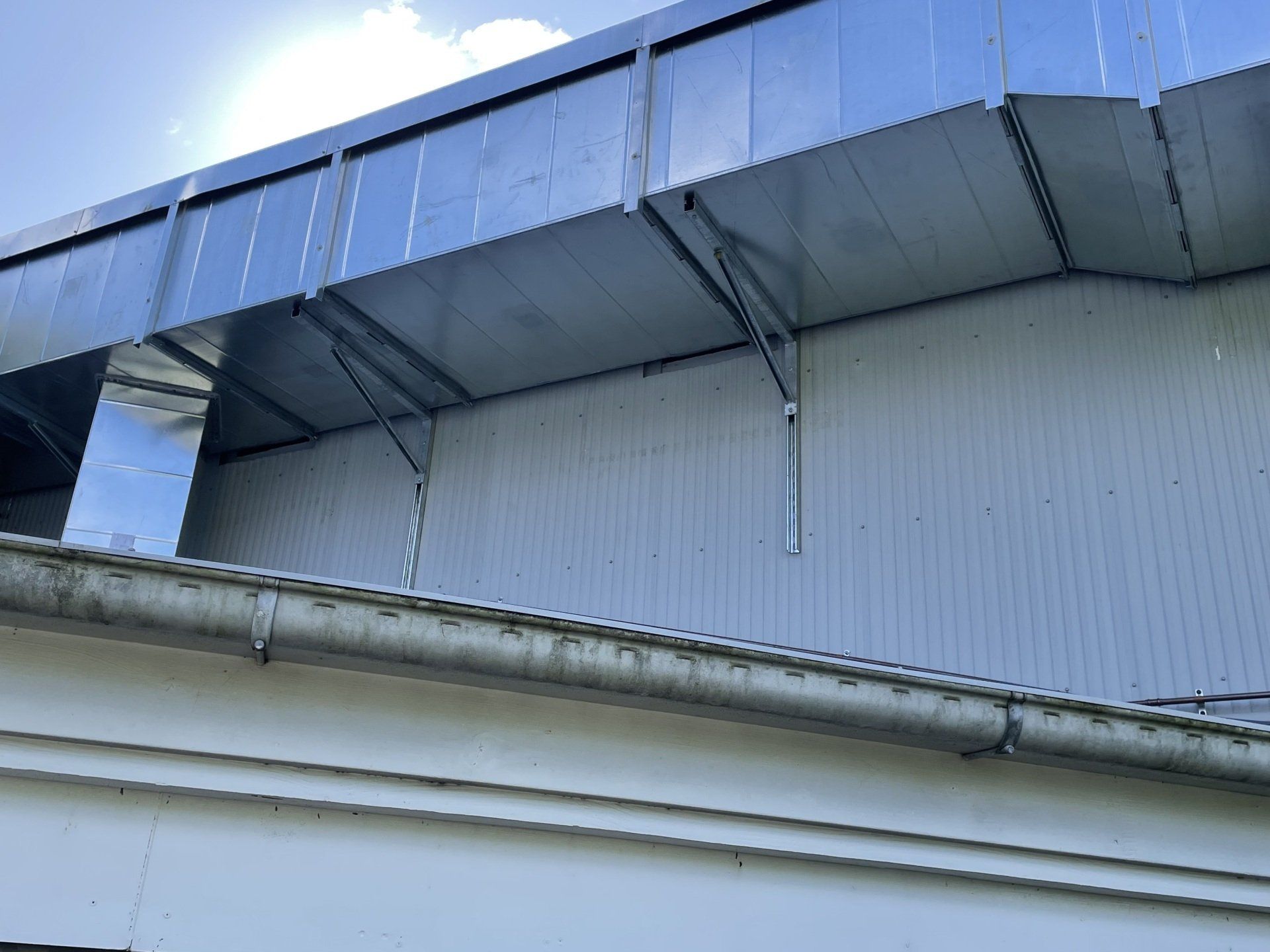 Industrial building exterior with blue metal awning and white corrugated wall under a cloudy sky