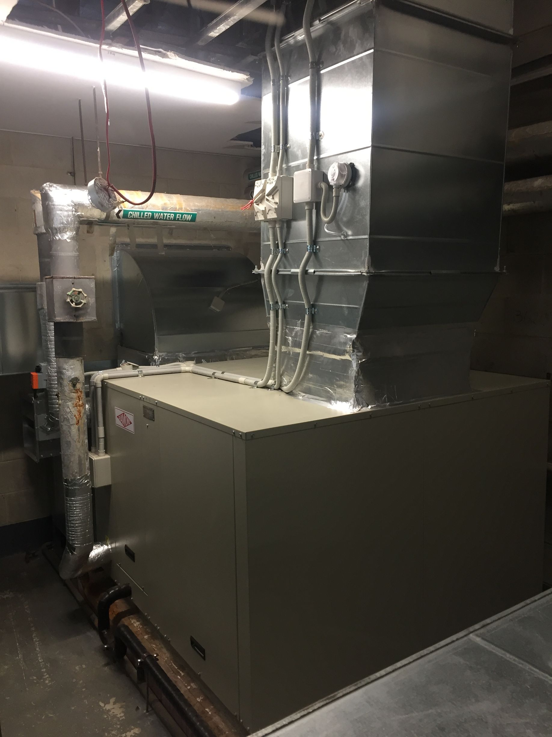 Large industrial HVAC unit in a metal mechanical room with insulated ductwork and pipes
