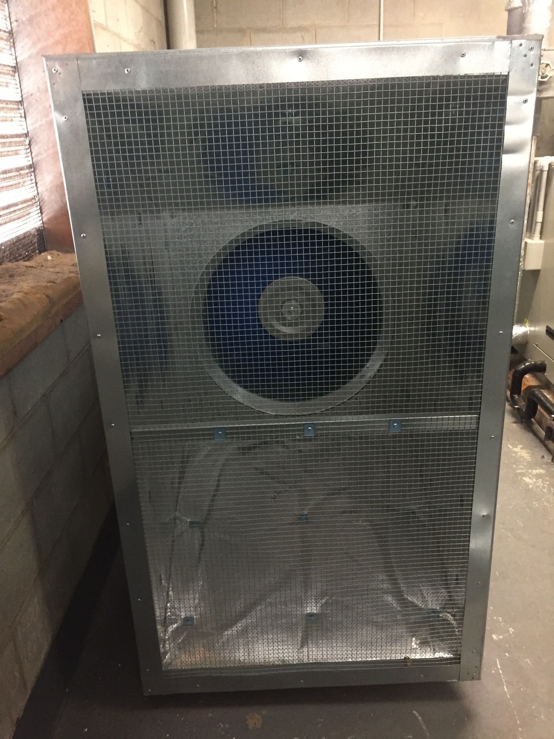 Large metal unit with reflective front panel and blue spiral design, standing indoors against a brick wall