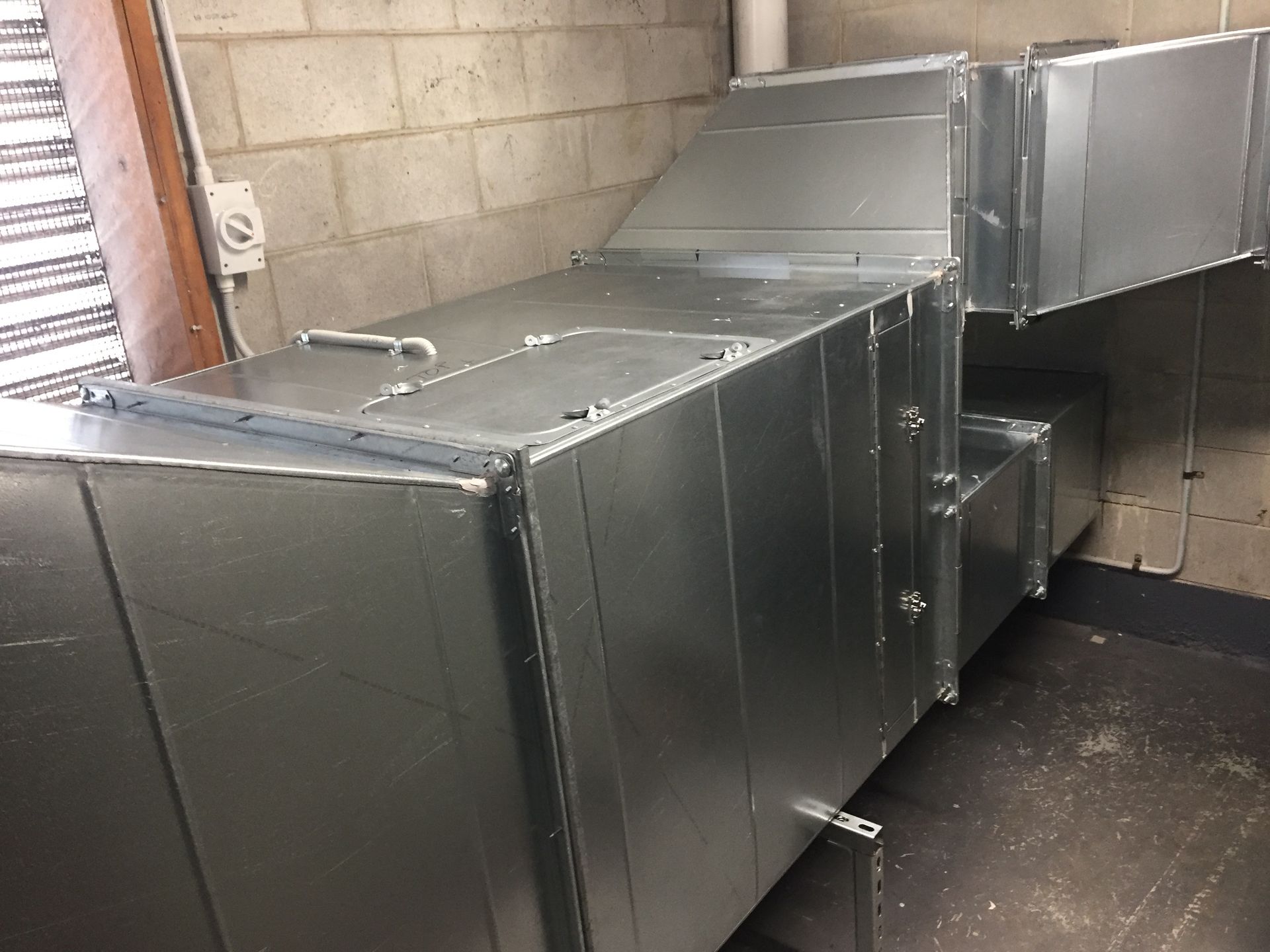 Metal HVAC ductwork and vents installed along a cinder block wall in a utility room