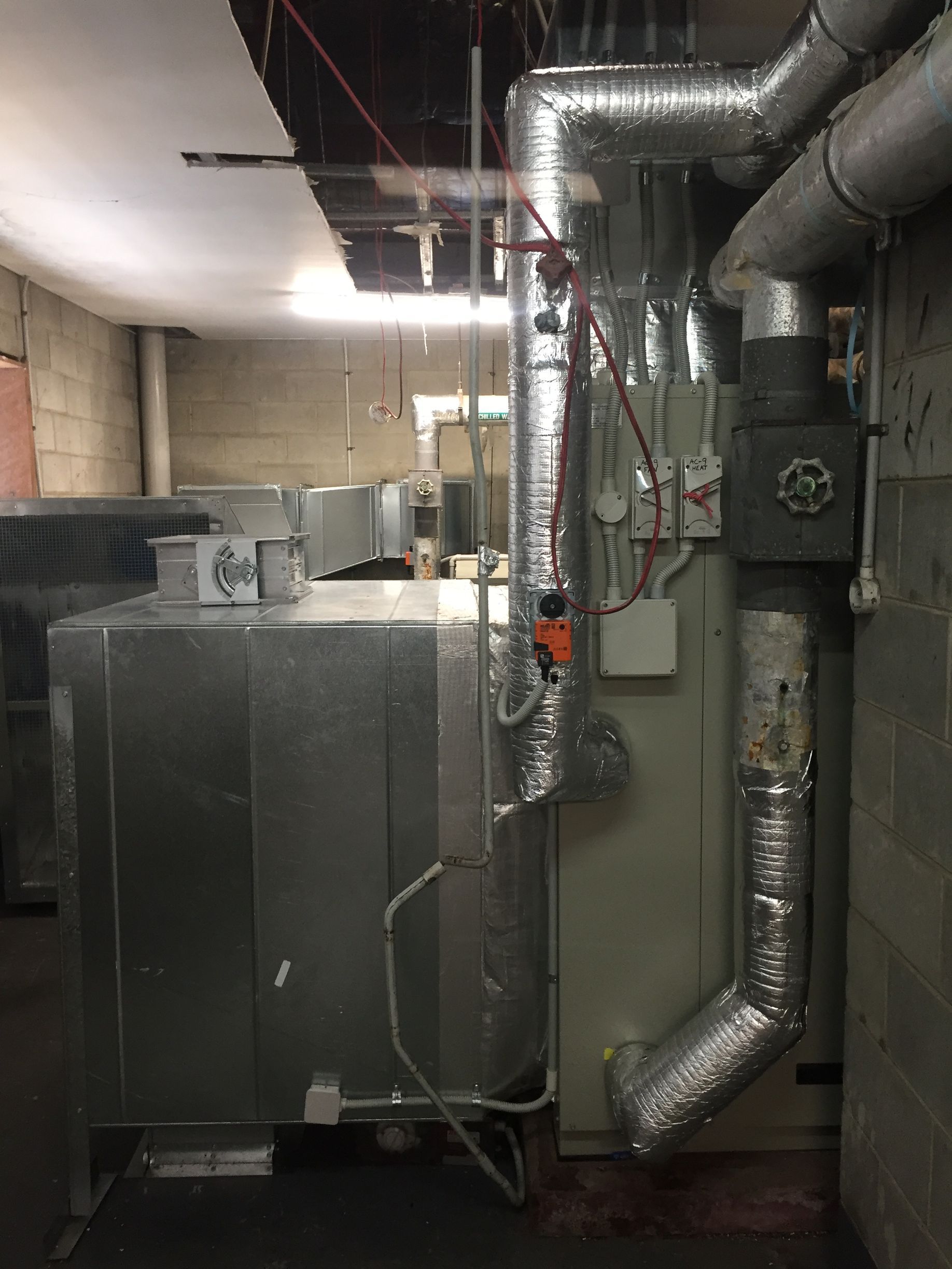 Basement utility room with large HVAC unit and silver insulated ductwork against concrete walls.