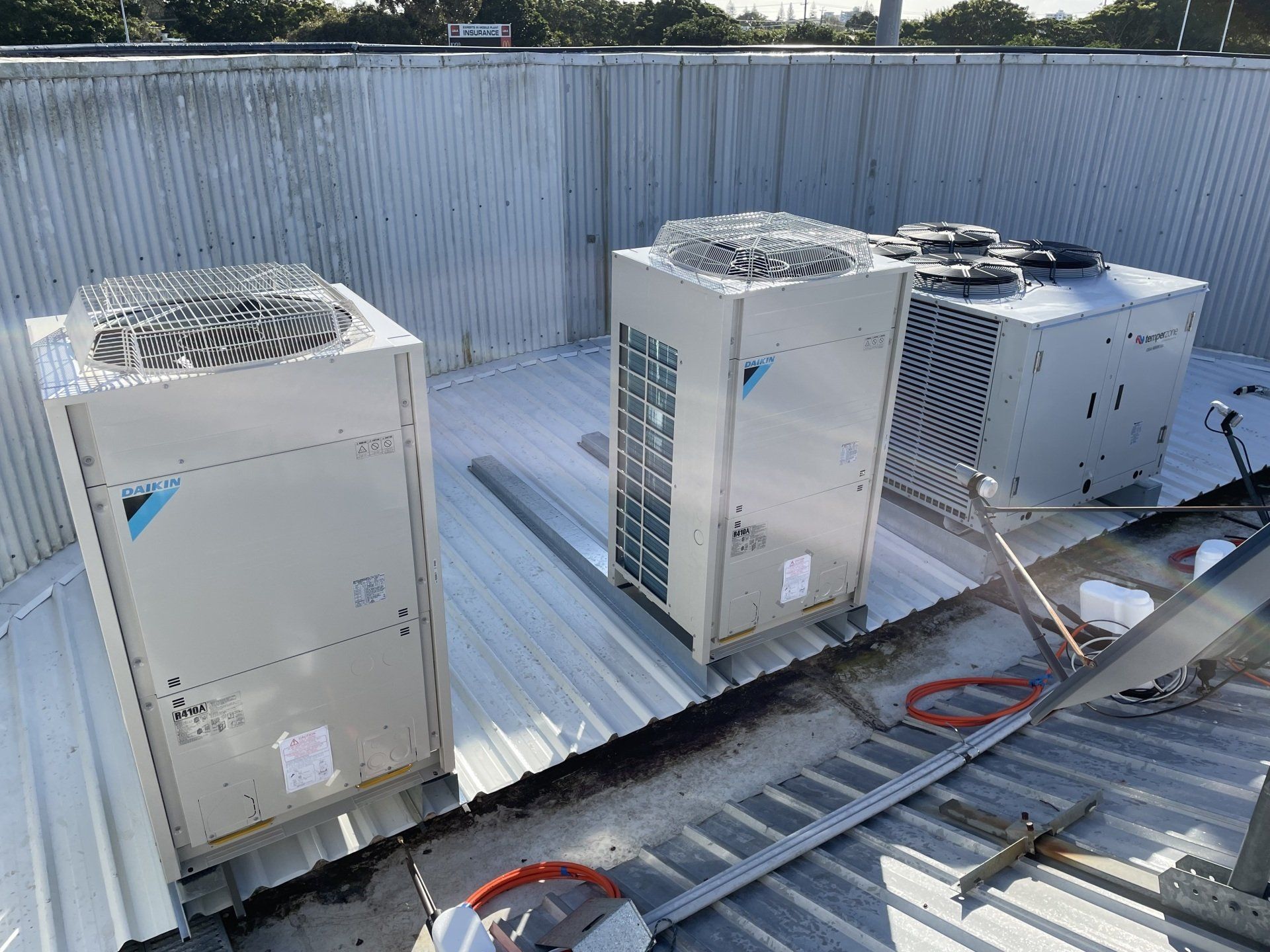 Three rooftop HVAC units on a corrugated metal roof with conduit and cables nearby