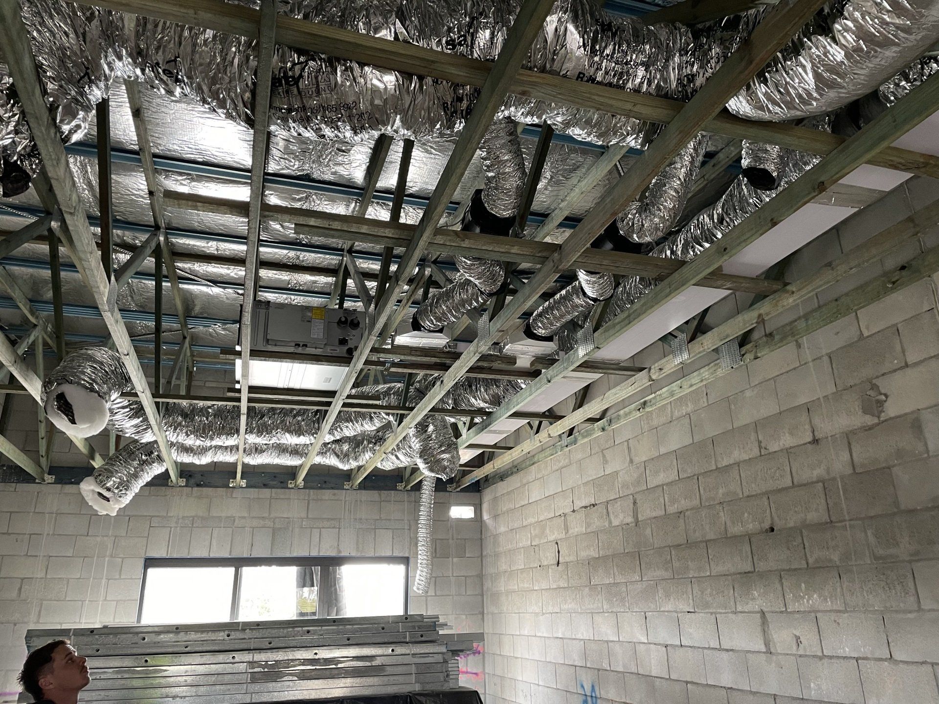 Unfinished room with concrete block walls and exposed ceiling beams, insulation, and wiring.