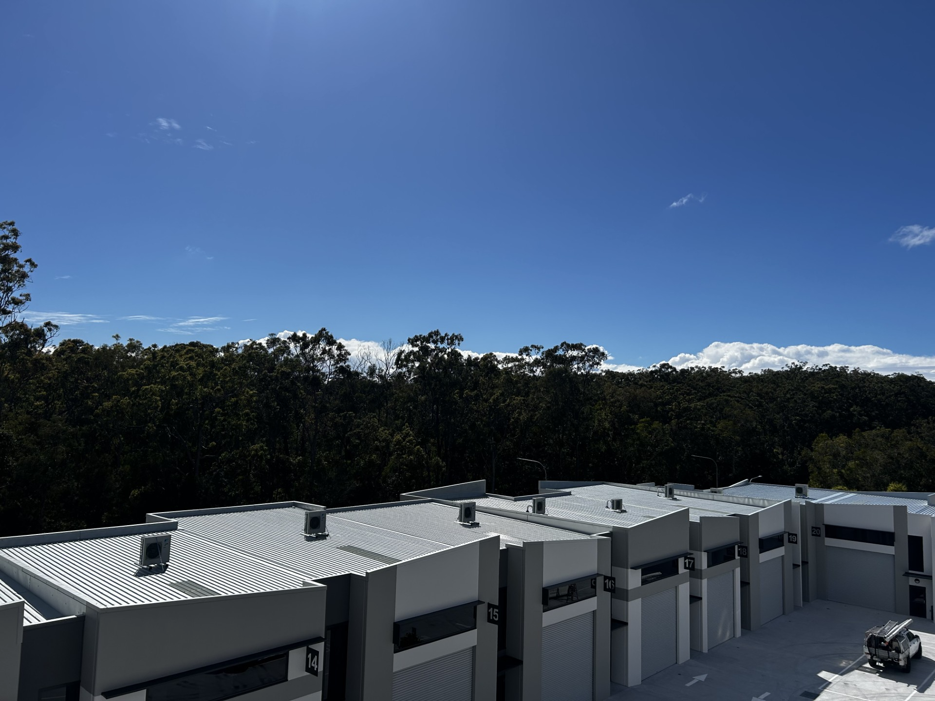Row of white flat-roof buildings under a clear blue sky with trees in the background
