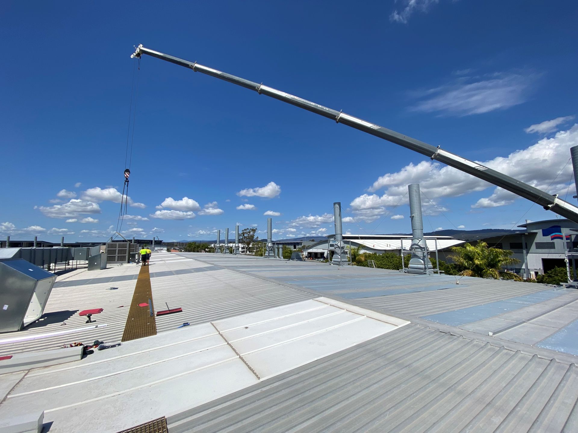 Construction site with a crane lifting materials over a corrugated metal roof under a bright blue sky