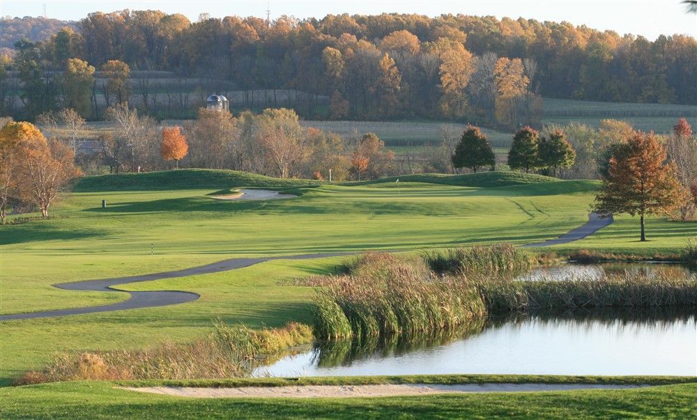 Golf course with pond, sand traps, and fall foliage in the background.