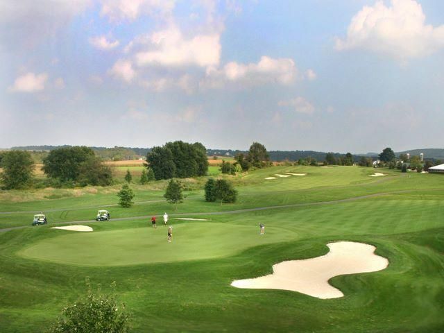 Golf course scene with green fairways, sand traps, and golfers under a cloudy sky.