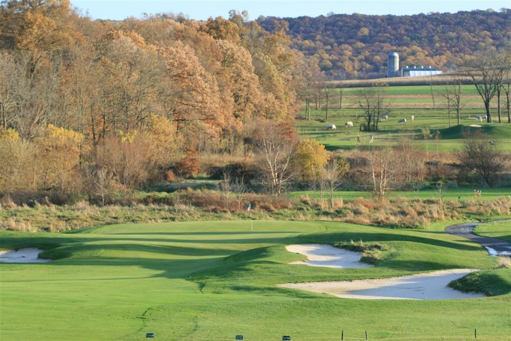 Golf course fairway with sand traps and trees in autumn colors; a distant barn.