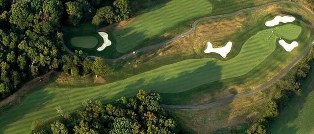 Aerial view of a golf course with green fairways, white sand traps, and trees.