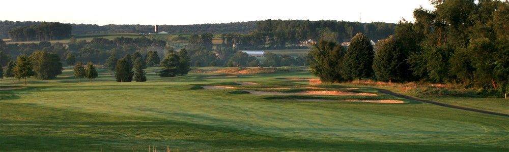 Green golf course with trees in the background under a light sky.