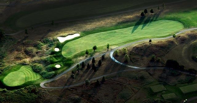 Aerial view of a golf course with green fairways, bunkers, and a winding road.