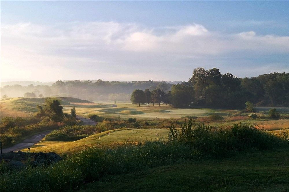 Golf course landscape with morning fog and sunlight. Green grass, trees, and blue sky.